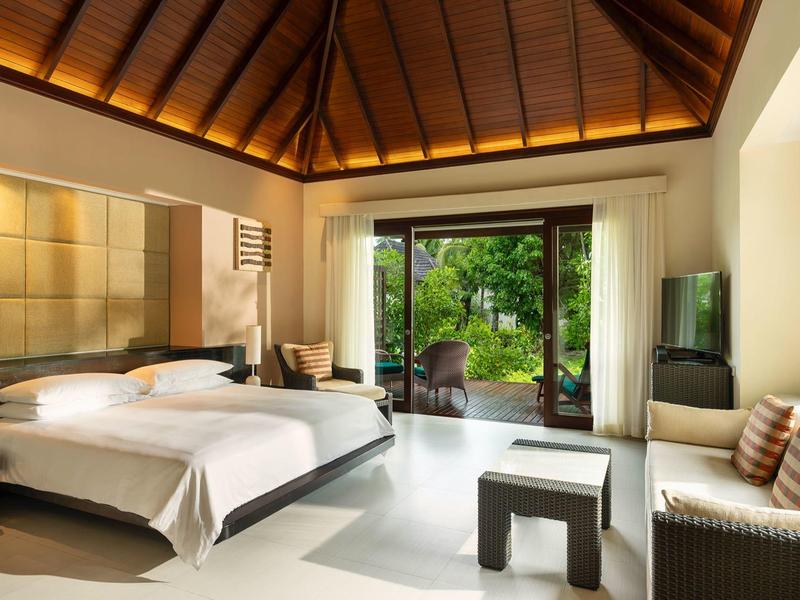 Modernes Hotelzimmer mit Doppelbett, Holzdecke und Blick auf einen grünen Garten.