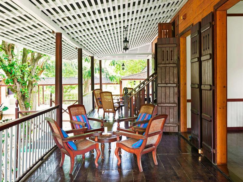 Überdachter Balkon mit Holzgeländer und bunten Stühlen neben einem Hotelzimmer.