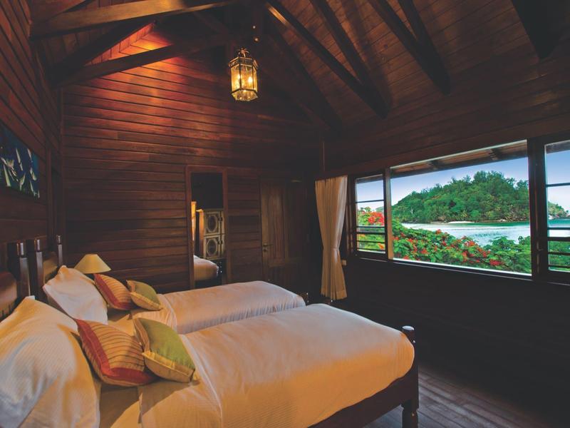Gemütliches Schlafzimmer mit Holzwänden, großem Fenster und Blick auf grüne Landschaft und Wasser.