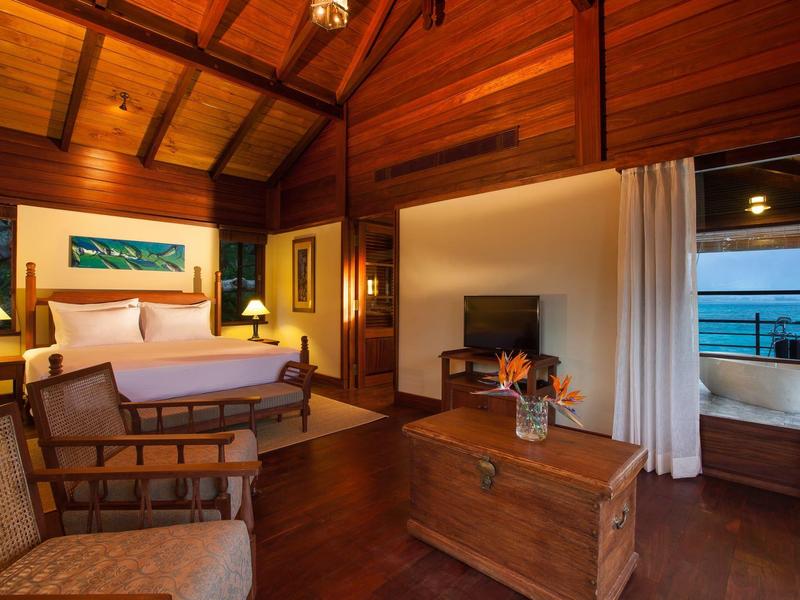 Gemütliches Holzschlafzimmer mit Doppelbett, Kamin und Blick auf das Meer durch offene Tür.