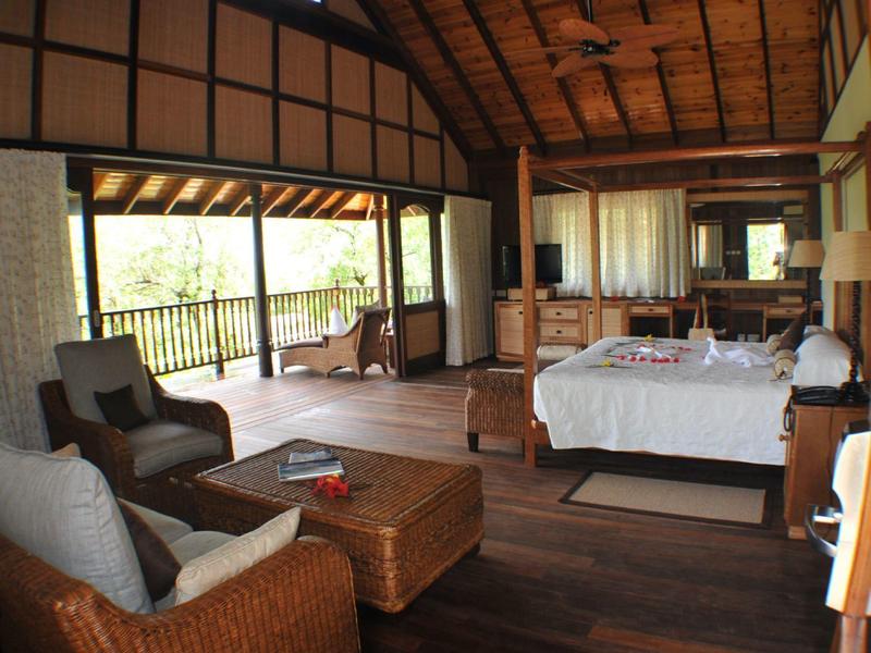 Spacious hotel room with bamboo furniture, wooden floor, and nature view.