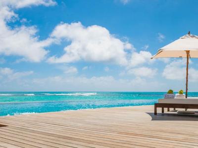 Entspannender Liegestuhl mit Sonnenschirm auf Holzsteg mit Blick auf das türkisfarbene Meer.