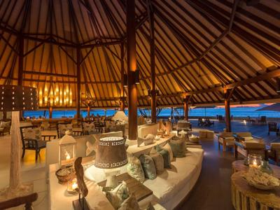 Offenes Restaurant mit Holzdach, gemütlichen Sitzbereichen und Meerblick bei Sonnenuntergang.