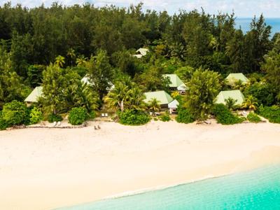 Tropischer Strand mit weißem Sand, türkisfarbenem Wasser und kleinen Hütten im dichten grünen Wald.