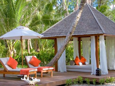 Holzterrasse mit Liegestühlen, Sonnenschirm und Pavillon, umgeben von tropischen Palmen.