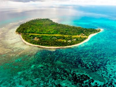 Grüne, bewaldete Insel mit weißem Sandstrand, umgeben von klarem, türkisfarbenem Meer und Korallenriffen.