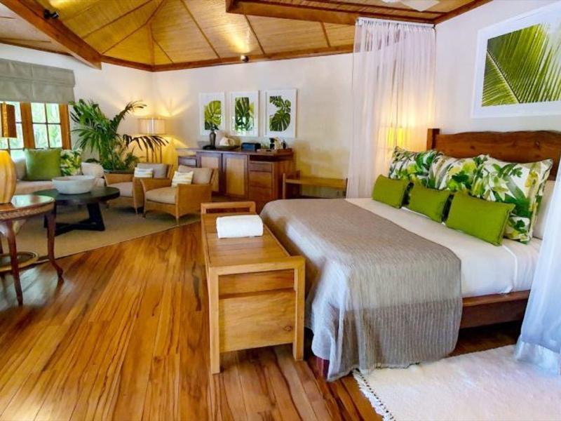 Großes Schlafzimmer mit Holzboden, Doppelbett, Pflanzen und moderner, heller Einrichtung.