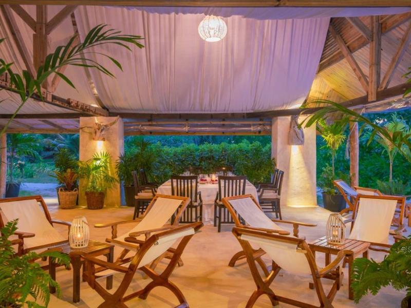 Gemütliche, offene Lounge mit Holzstühlen, Pflanzen und warmem Licht in tropischem Ambiente.