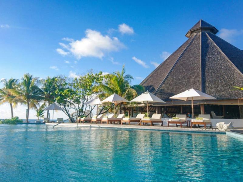 Strandresort mit großem Pool, Palmen und pyramidenförmigem Gebäude bei klarem Himmel.