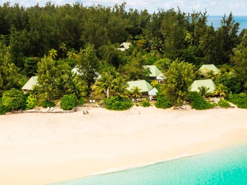 Tropischer Strand mit weißem Sand, türkisfarbenem Wasser und kleinen Hütten im dichten grünen Wald.