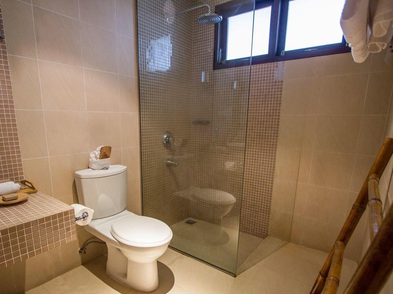 Moderne Badezimmerecke mit weißer Toilette, Glasdusche und beiger Fliesenverkleidung.