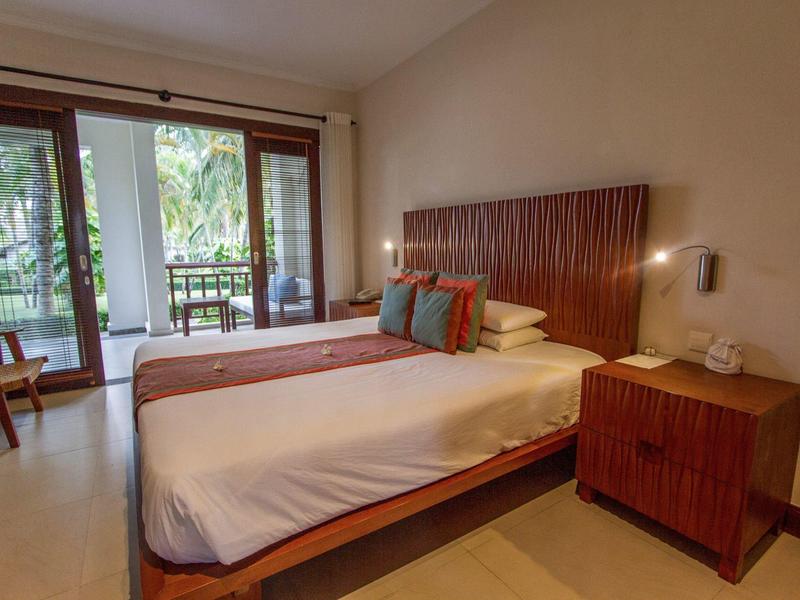 Modernes Hotelzimmer mit zwei Einzelbetten, Holzmöbeln und Zugang zu einem Balkon mit Grünblick.