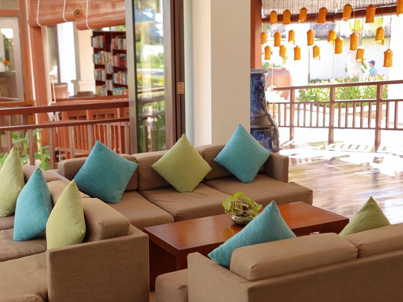 Gemütliche Lounge mit beigen Sofas und bunten Kissen, Holztische und große Fenster, viel Tageslicht.