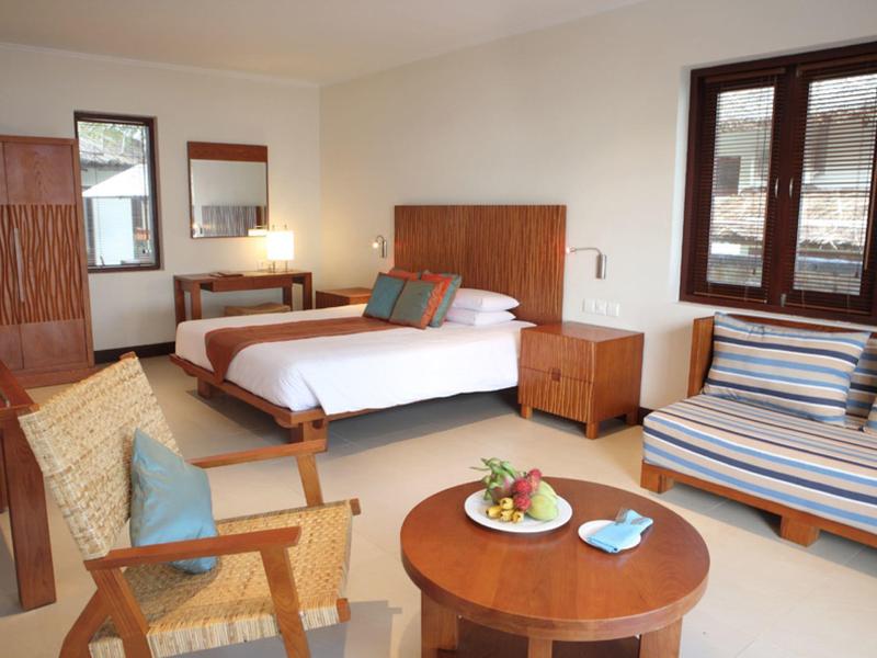 Helles Schlafzimmer mit großem Bett, Holzmöbeln, Sofa, Sesseln und rundem Couchtisch mit Obstkorb.