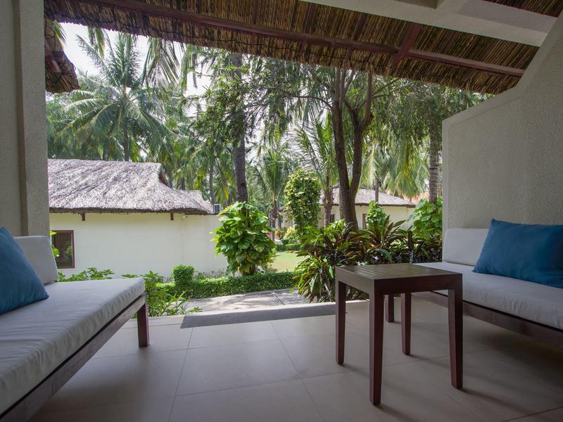 Offene Veranda mit zwei weißen Sofas, blauen Kissen, kleinem Holztisch und Blick auf Palmen.
