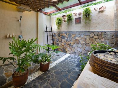 Hotelové nádvoří s kamennou podlahou, zelenými rostlinami a venkovní sprchou za denního světla.