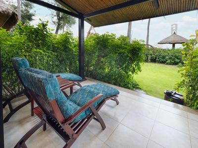 Dva polstrované lehátka na kryté terase s výhledem na zahradu a altán s deštníkem.