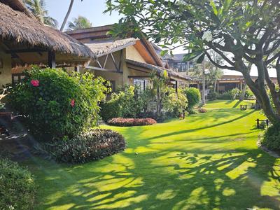 Zelená zahradní plocha s bungalovy a stíny stromů za slunečného počasí.