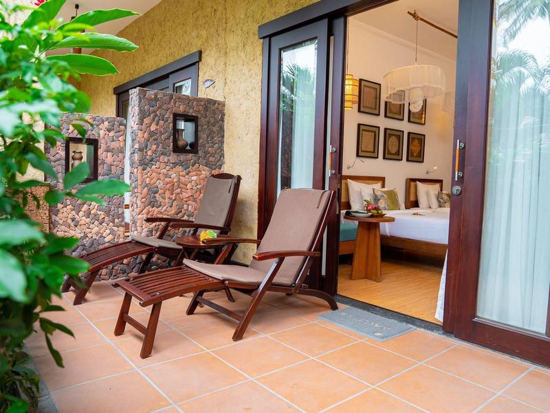 Balkon se dvěma lehátky, rostlinami a výhledem do pokoje s manželskou postelí.