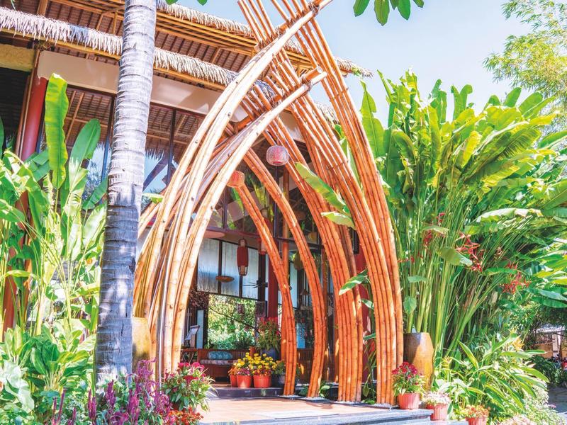 Vstup do tropického hotelu s dekorativními bambusovými oblouky a bujnou zelenou vegetací.