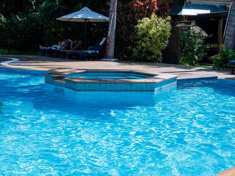 Vyhřívaná vířivka s modrou vodou v bazénu a slunečními parasoly v pozadí