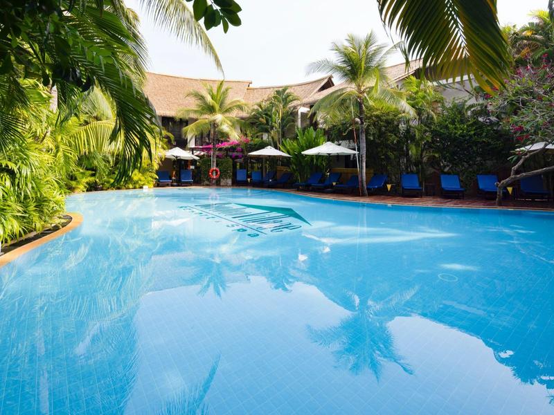 Velký bazén obklopený palmami a lehátky v tropickém hotelovém prostředí.