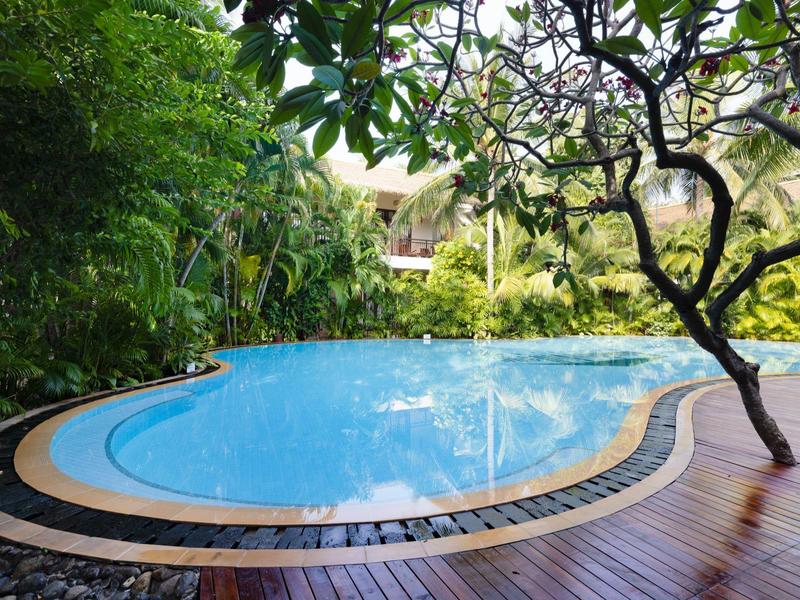 Kulatý bazén v tropické zahradě s dřevěnou terasou a bujnou zelení.