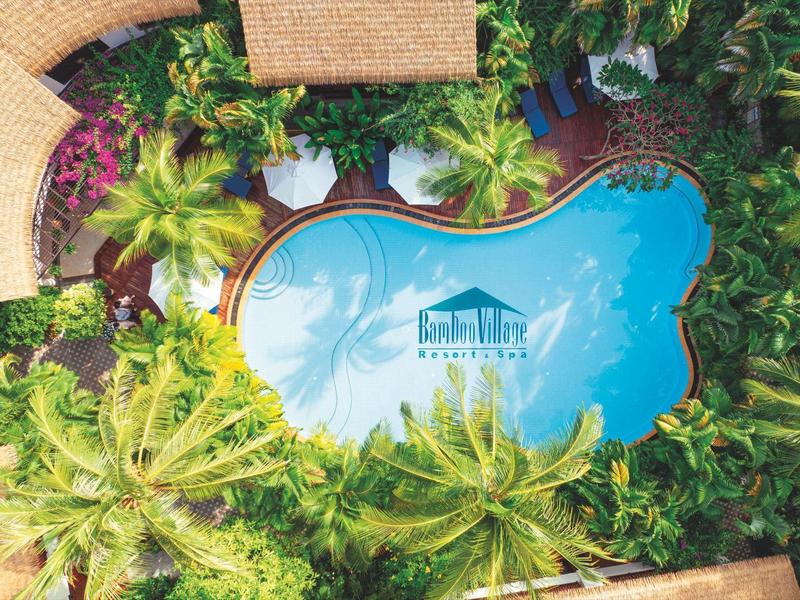 Letecký pohled na tropický bazén obklopený palmami a bujnou vegetací.