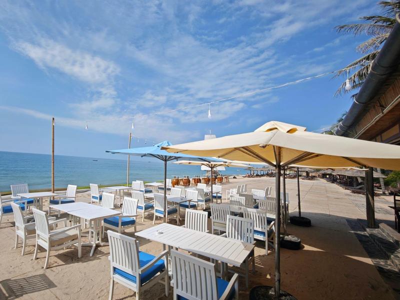 Plážová terasa s bílými židlemi a slunečníky za modrou oblohou a mořem.