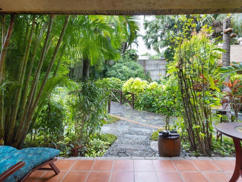 Zastřešená terasa s výhledem na zahradu a polstrovanou židlí pod bambusy.