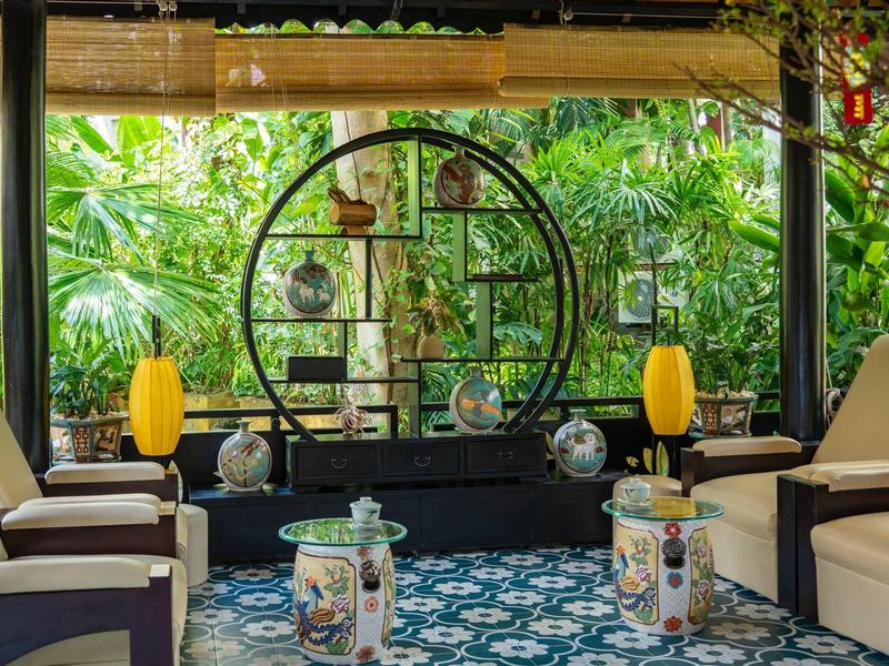 Lounge s křesly, dekorativními stolky a tropickou zelení v pozadí.