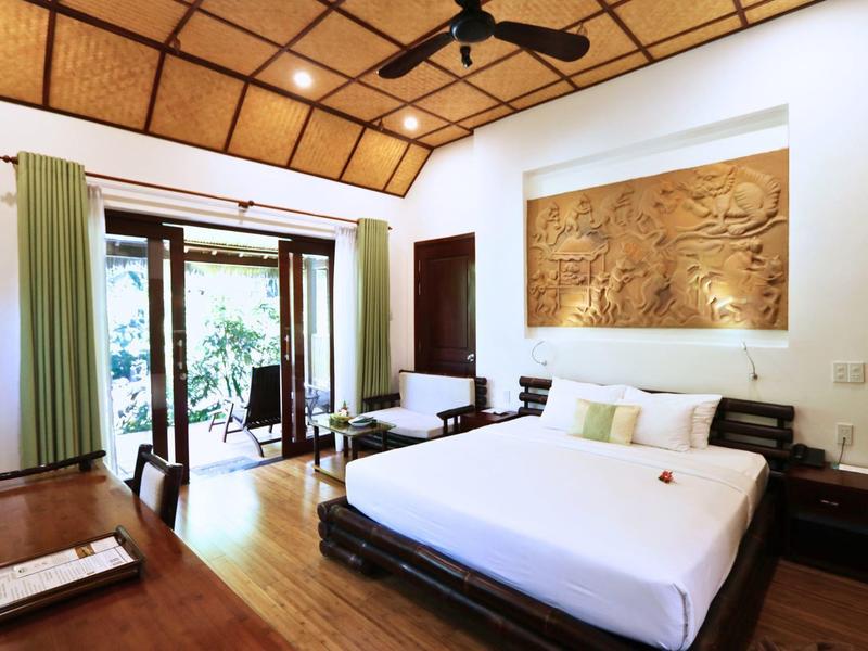 Světý hotelový pokoj s velkou postelí, dřevěným stropem a přístupem na balkon s výhledem do zahrady.