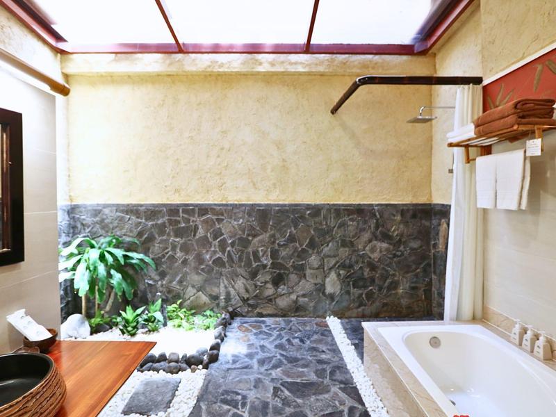 Světlá koupelna s vanou, kamennou podlahou a rostlinami pod skleněnou střechou.