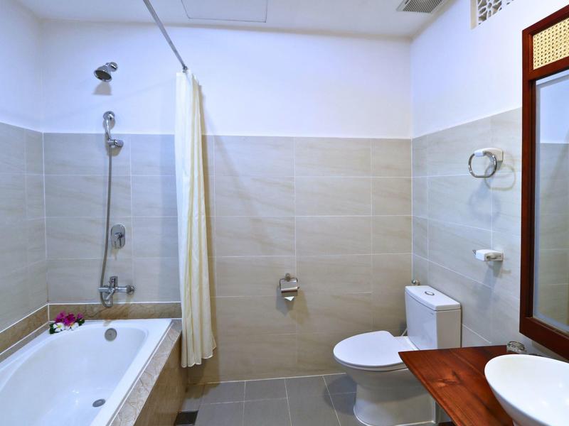 Světla koupelna s vanou, sprchovým závěsem, toaletou a dřevěnou umyvadlovou skříňkou se zrcadlem.