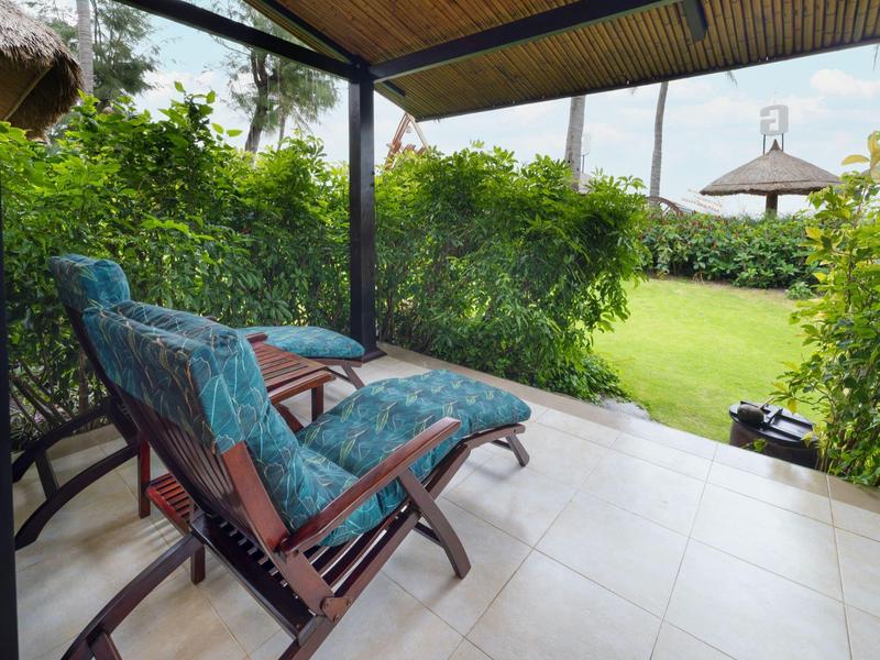 Dva polstrované lehátka na kryté terase s výhledem na zahradu a altán s deštníkem.