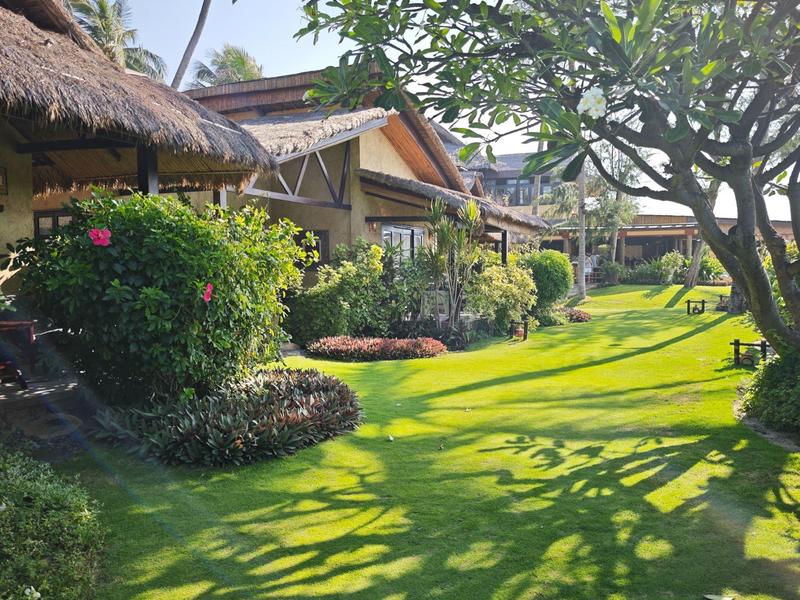 Zelená zahradní plocha s bungalovy a stíny stromů za slunečného počasí.