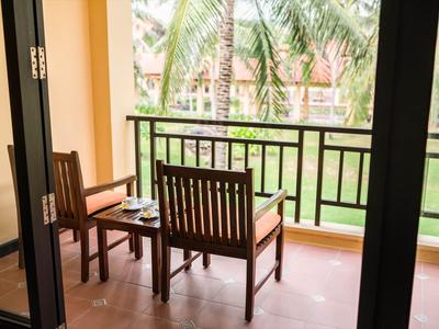 Balcon avec mobilier en bois donnant sur un jardin verdoyant avec des palmiers.