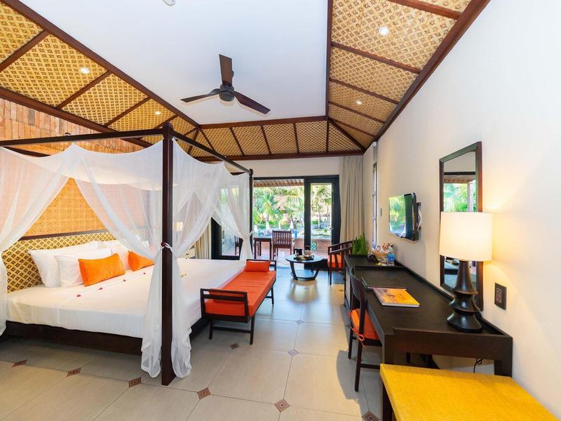 Lichte hotelkamer met hemelbed, bureau, stoelen en uitzicht op de tuin.