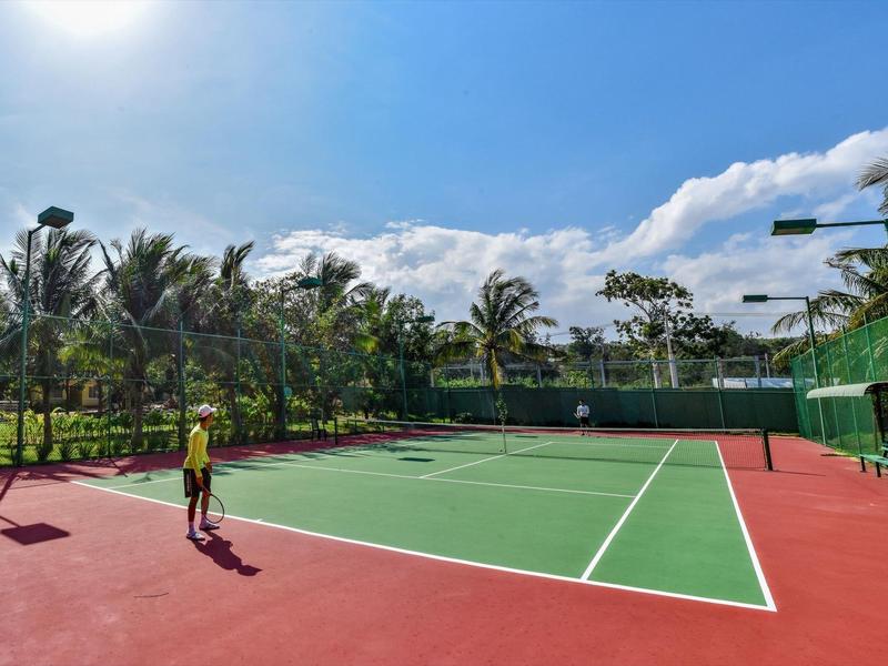 Buiten tennisbaan met palmbomen en persoon onder zonnige hemel.