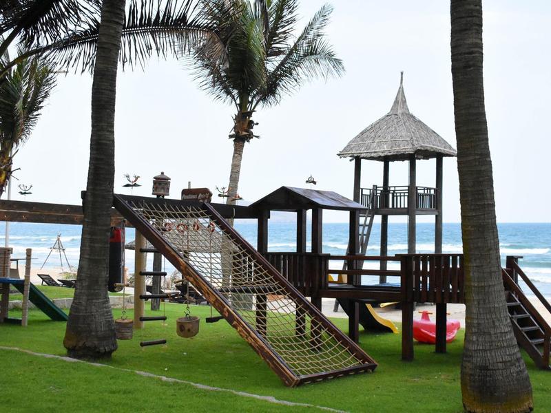 Speeltuin voor kinderen met glijbaan en klimnet naast palmbomen en uitzicht op zee bij hotel