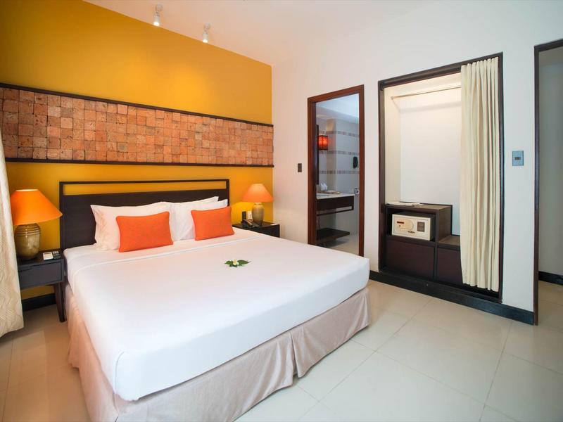 Moderne hotelkamer met groot bed, oranje kussens en kluis in de kast.