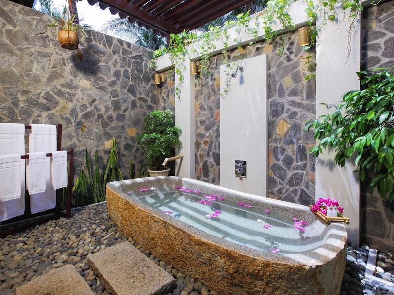 Vrijstaande stenen badkuip in een open badkamer versierd met planten.