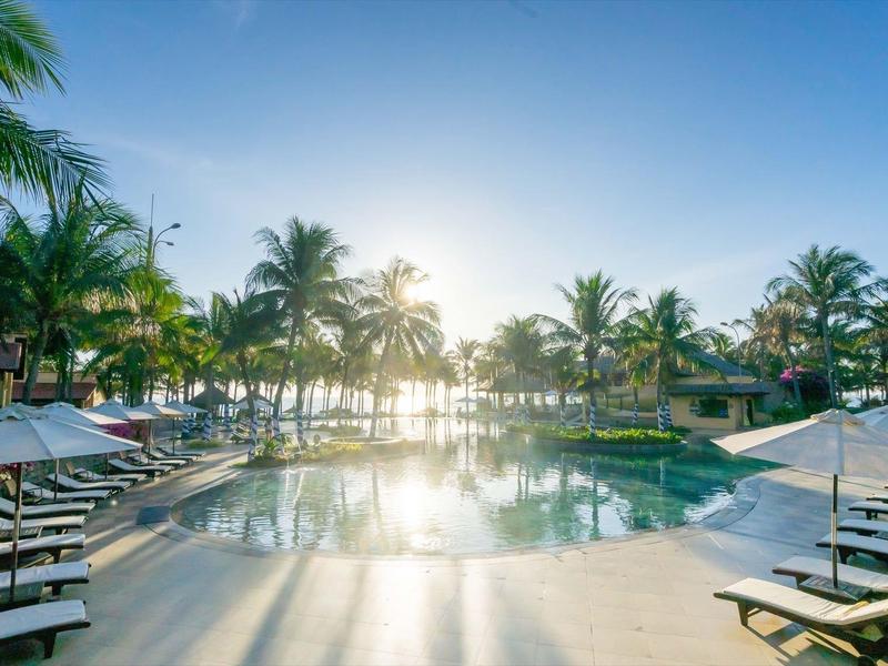 Hotelzwembad met ligstoelen en palmbomen bij zonsondergang aan zee