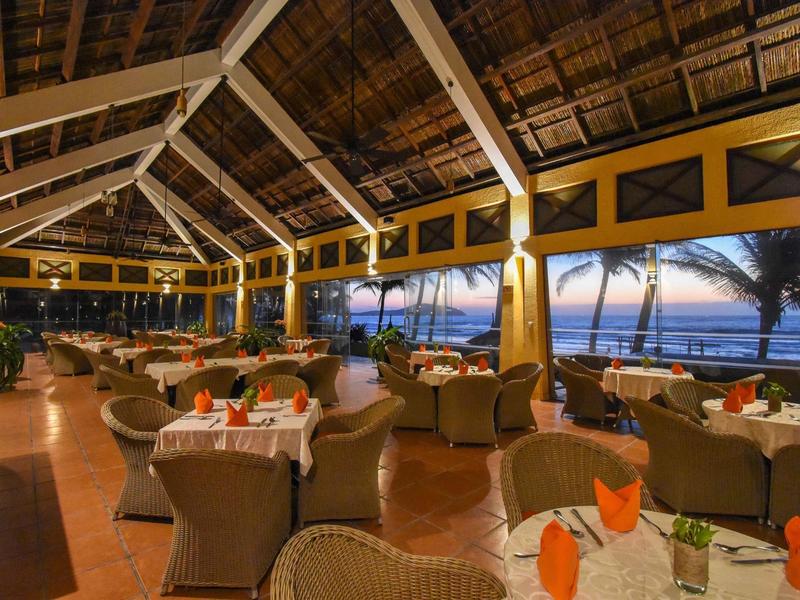 Open eetruimte met rotanmeubilair met uitzicht op tropisch strand bij zonsondergang.