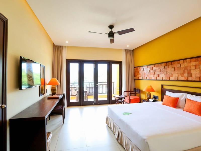 Lichte hotelkamer met groot bed, tv en balkon met uitzicht naar buiten.