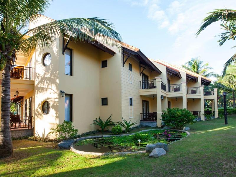 Hotelgebouw met balkons omgeven door palmbomen op een groen gazon bij daglicht.