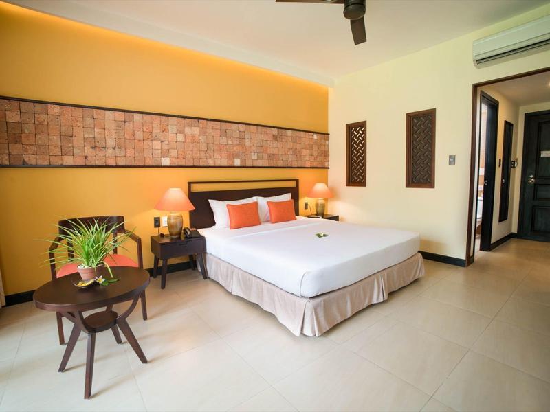 Lichte, moderne hotelkamer met groot bed, decoratieve kussens en een kleine tafel met een plant.