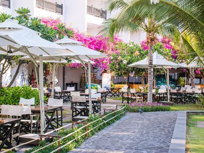 Strefa zewnętrzna hotelu z stołami, krzesłami, parasolami i kwitnącymi pnączami bugenwilli.