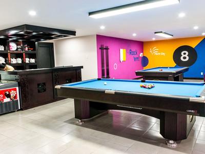 Dwie osoby grają w tenisa na niebieskim boisku na świeżym powietrzu otoczonym drzewami i zielonymi ogrodzeniami.