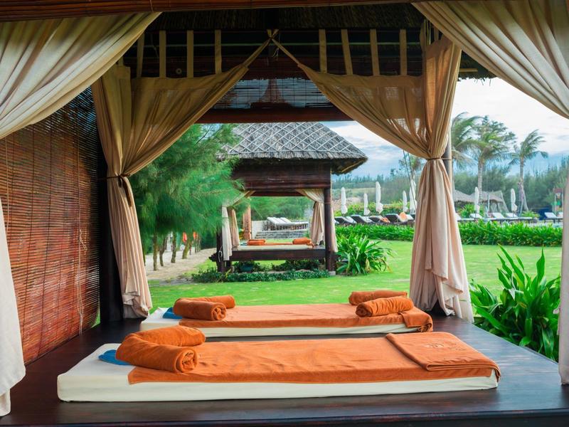 Otwarta ogród z leżakami i zasłonami, otoczony zielenią i palmami.